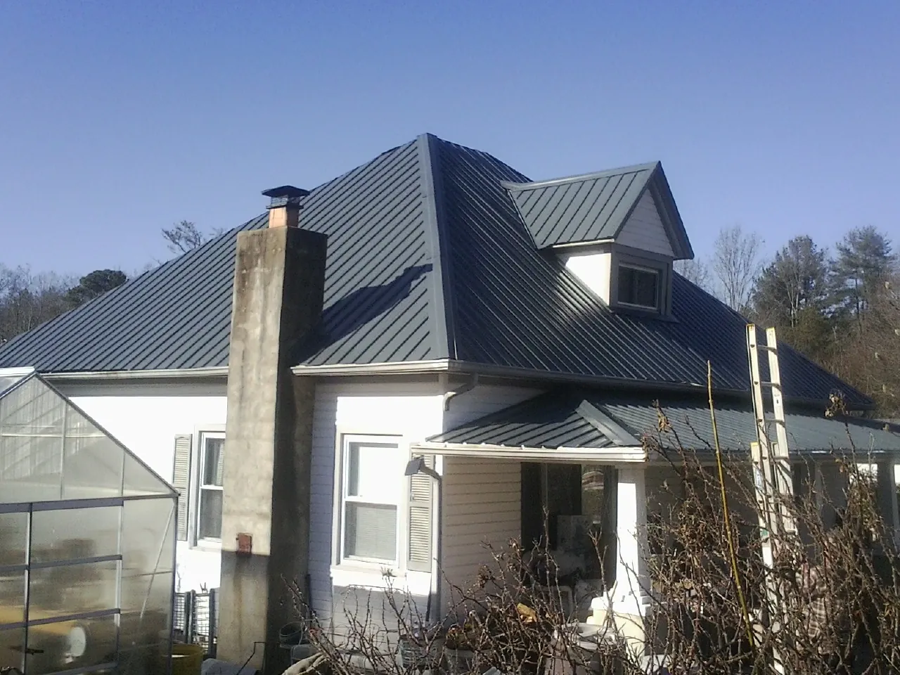 Dark blue standing seam metal roof on a white farmhouse with dormer — Slate & Tile Roof Repair by Roofing Brothers in Cambridge Springs