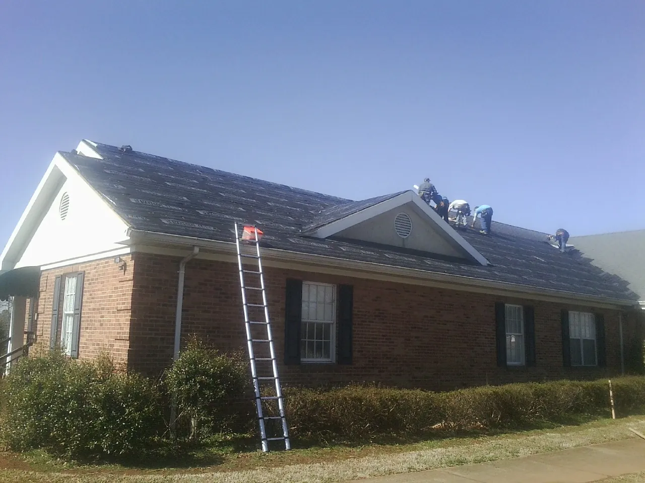 Crew tearing shingles off a brick ranch roof with a ladder set — Emergency Roof Repair work by our crew in Cambridge Springs