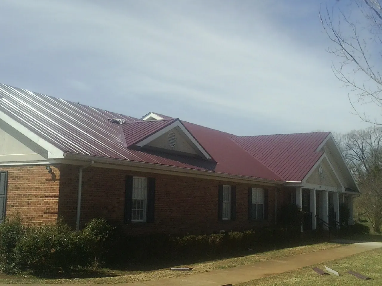 Red metal roof with gabled entries on a long brick building, from a Hail Damage Roof Repair job in Cambridge Springs