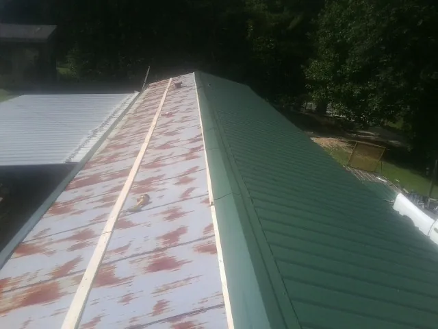 Old rusted panels beside newly installed green metal roofing — Wind Damage Roof Repair by Roofing Brothers in Cambridge Springs