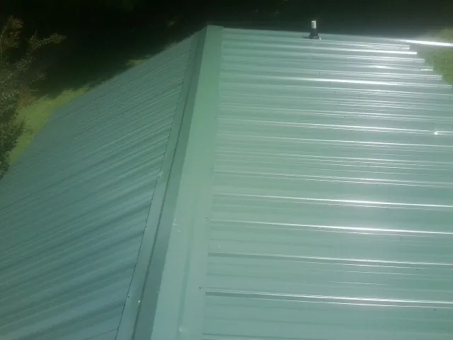 New green metal panels meeting at the ridge of a roof — Flat Roof Repair work by our crew in Cambridge Springs