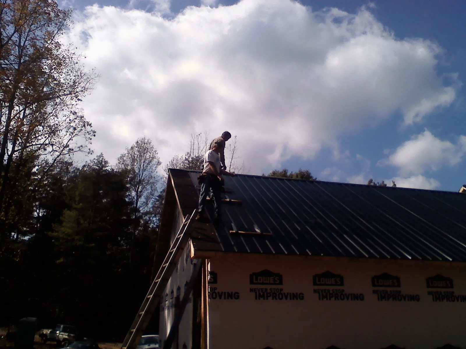 Roofer fastening dark metal panels high against a cloudy sky, from a Roof Inspection job in Cambridge Springs