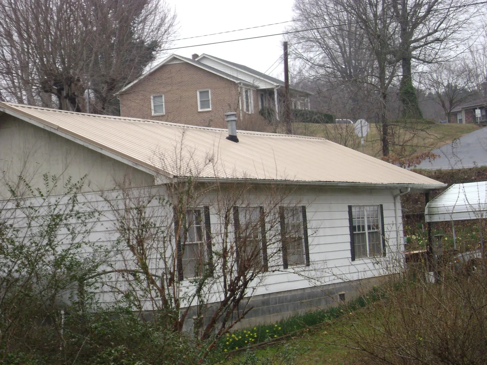 Tan metal roof on a white sided house set into a hillside — Commercial Roofing by Roofing Brothers in Cambridge Springs