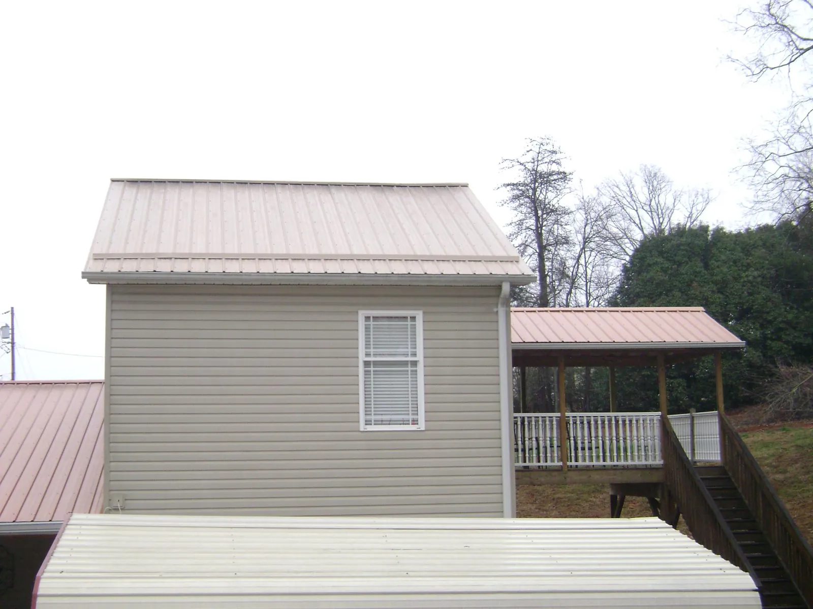 Tan metal roofs on a two story addition and attached porch, from a Roof Replacement job in Cambridge Springs