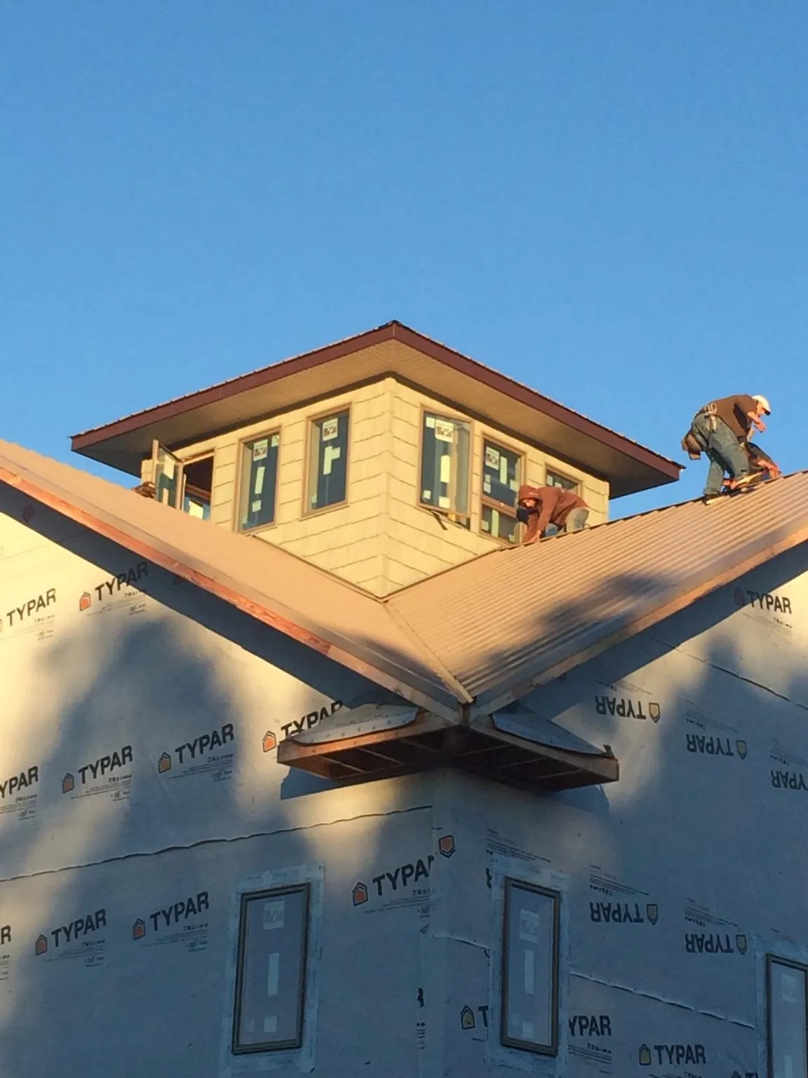 Roofers working around a rooftop cupola on a new metal roof at sunset — Roof Waterproofing in Cambridge Springs by Roofing Brothers